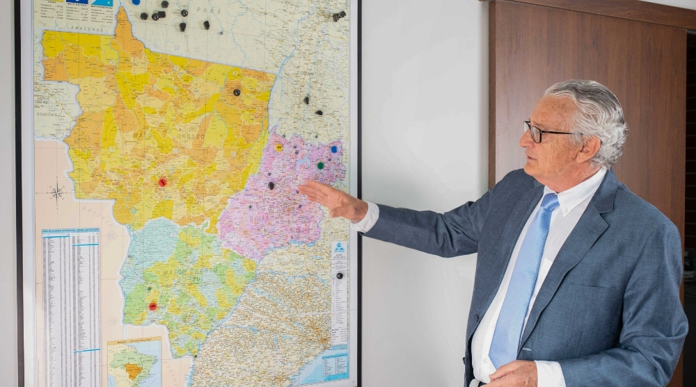 Luiz Antônio Vessani, presidente do Sindicato da Indústria da Mineração (MINDE), de terno e óculos, apontando para um grande mapa geológico de Goiás fixado na parede.
